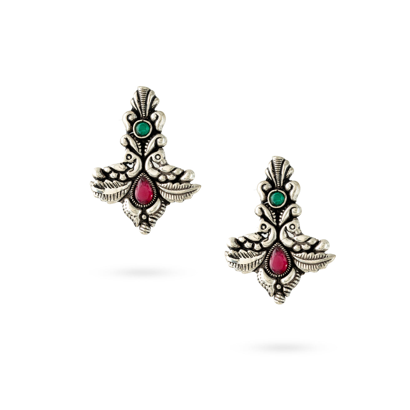 A pair of oxidized silver twin peacock earrings with intricate detailing and vibrant green and pink stones against a white background.