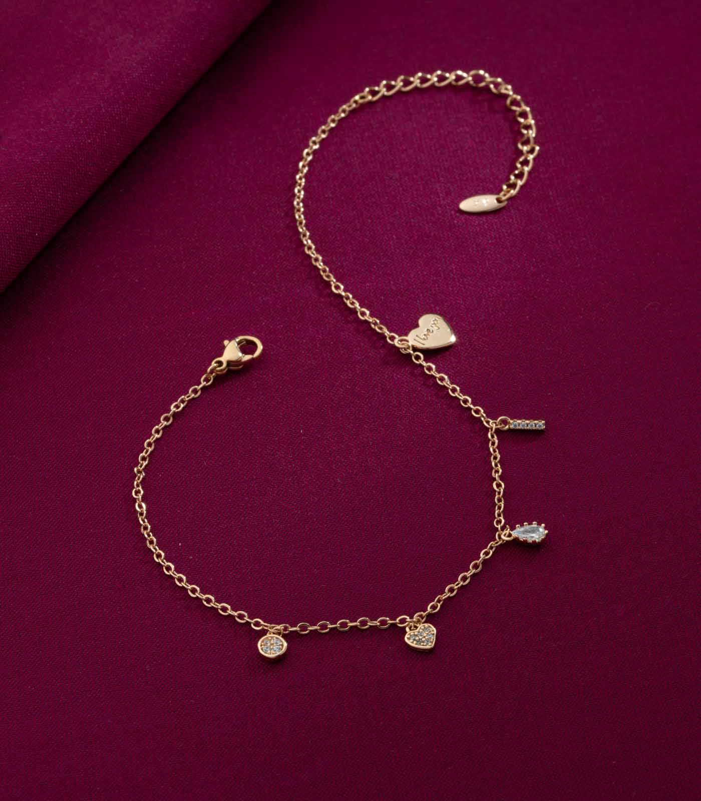 Gold bracelet with heart and round charms on a purple fabric background
