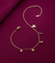 Gold bracelet with heart and round charms on a purple fabric background