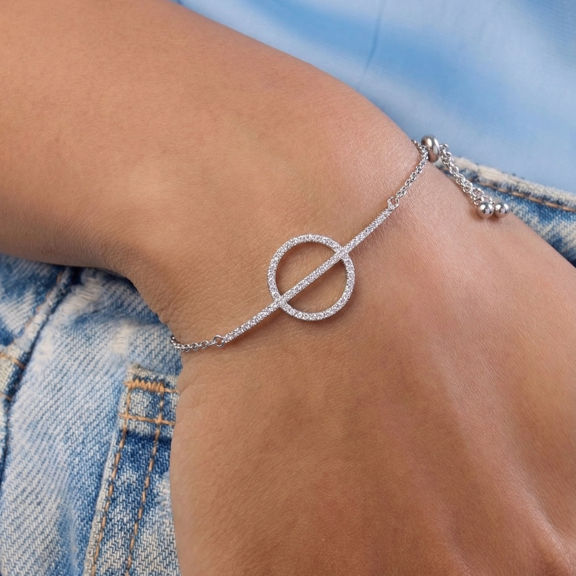 Silver bracelet with a circular design on a wrist, wearing denim jeans.