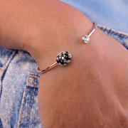 Close-up of a person's wrist wearing a rose gold bracelet with a gemstone on a denim background.