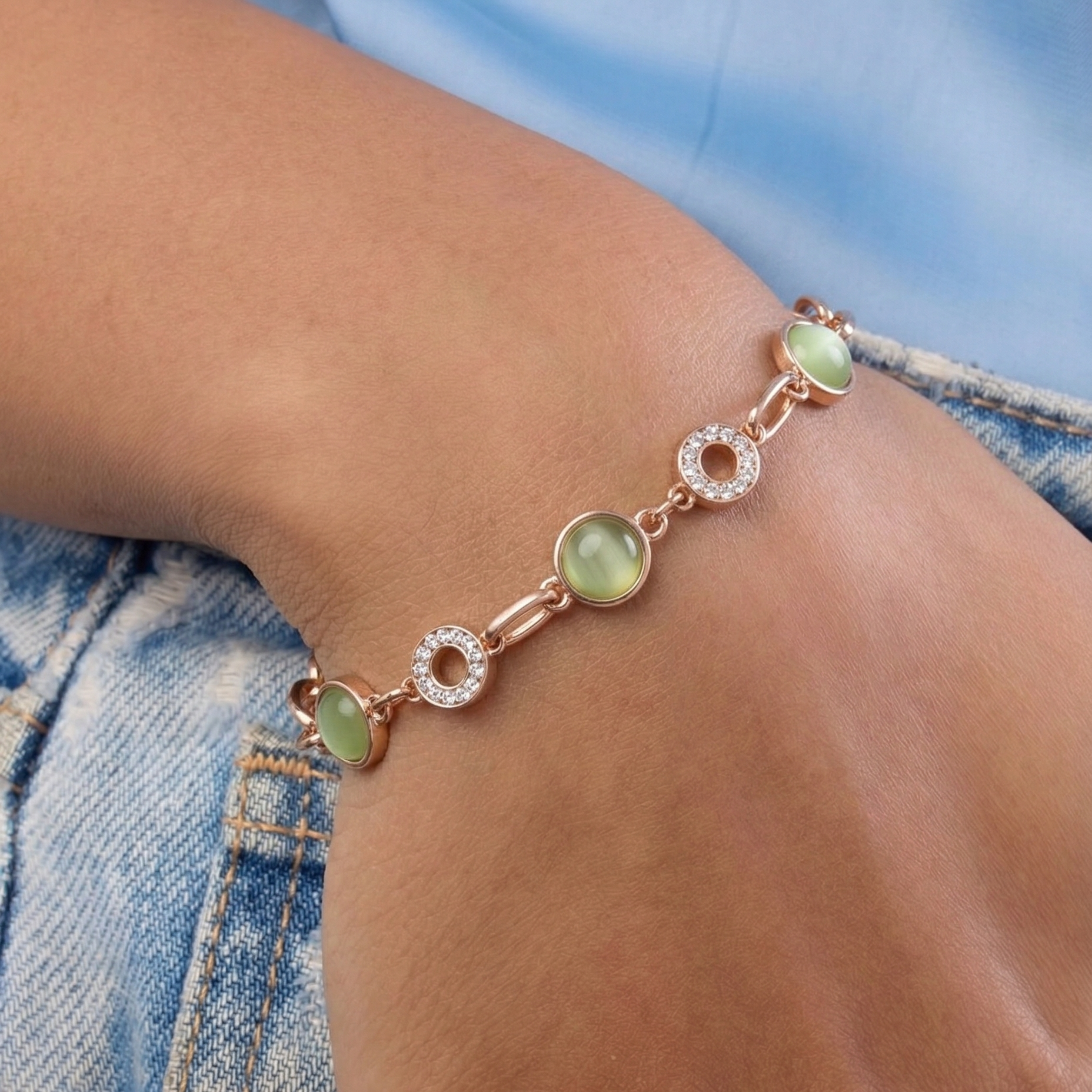 Bracelet with green gemstones and rose gold accents on a wrist against a denim background