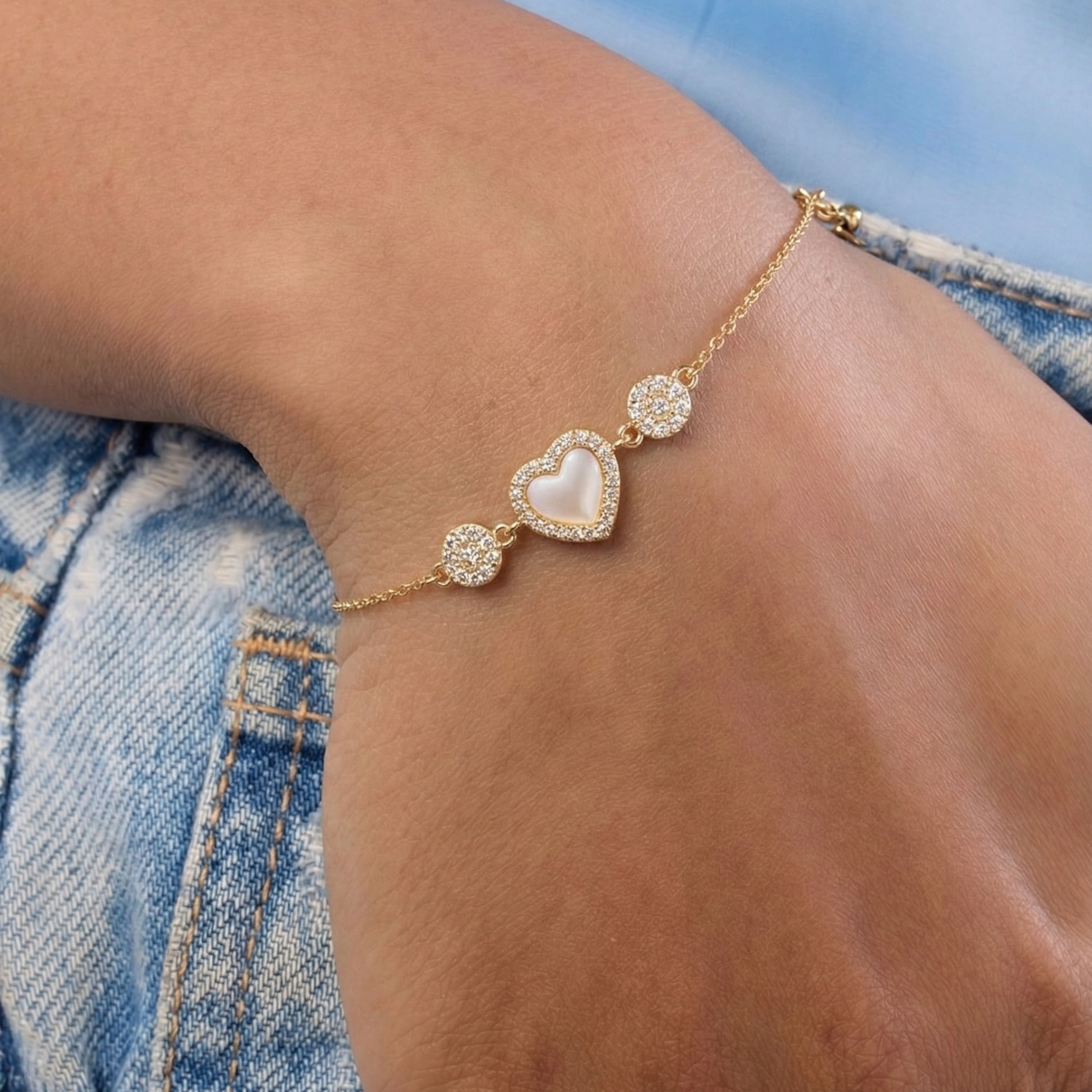 Gold bracelet with a heart-shaped gemstone on a wrist against a denim background