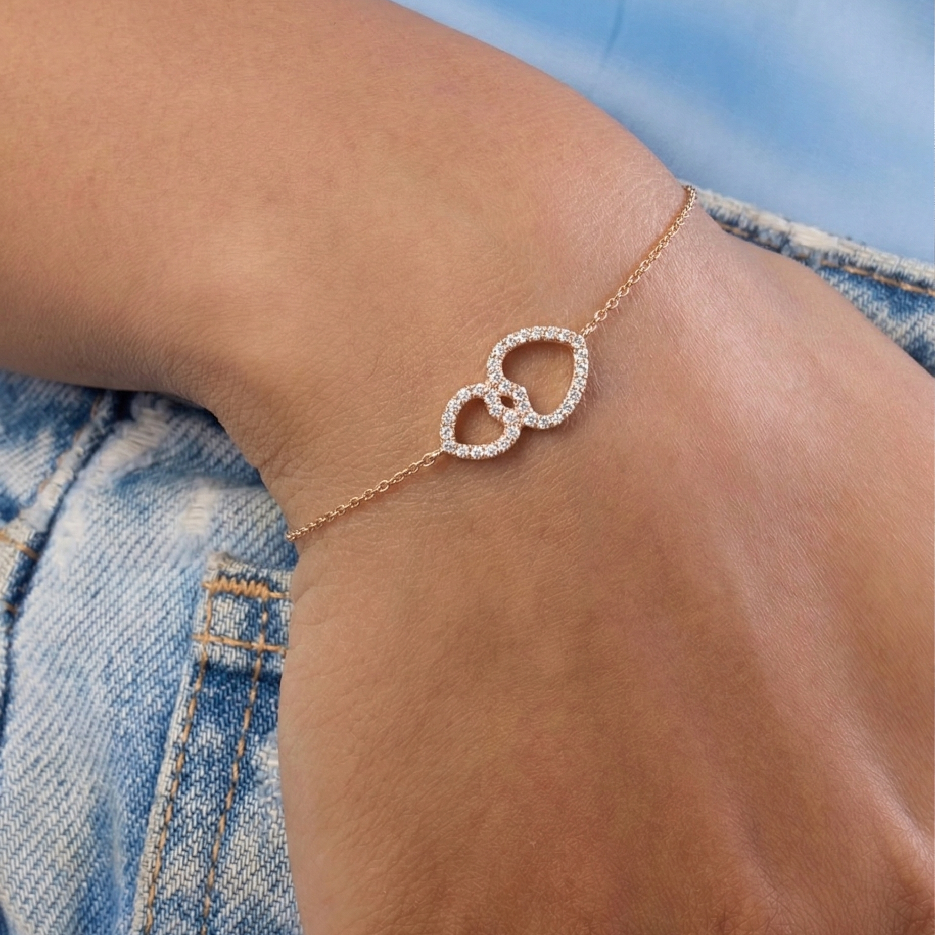 Rose gold bracelet with heart design on a wrist against a denim background