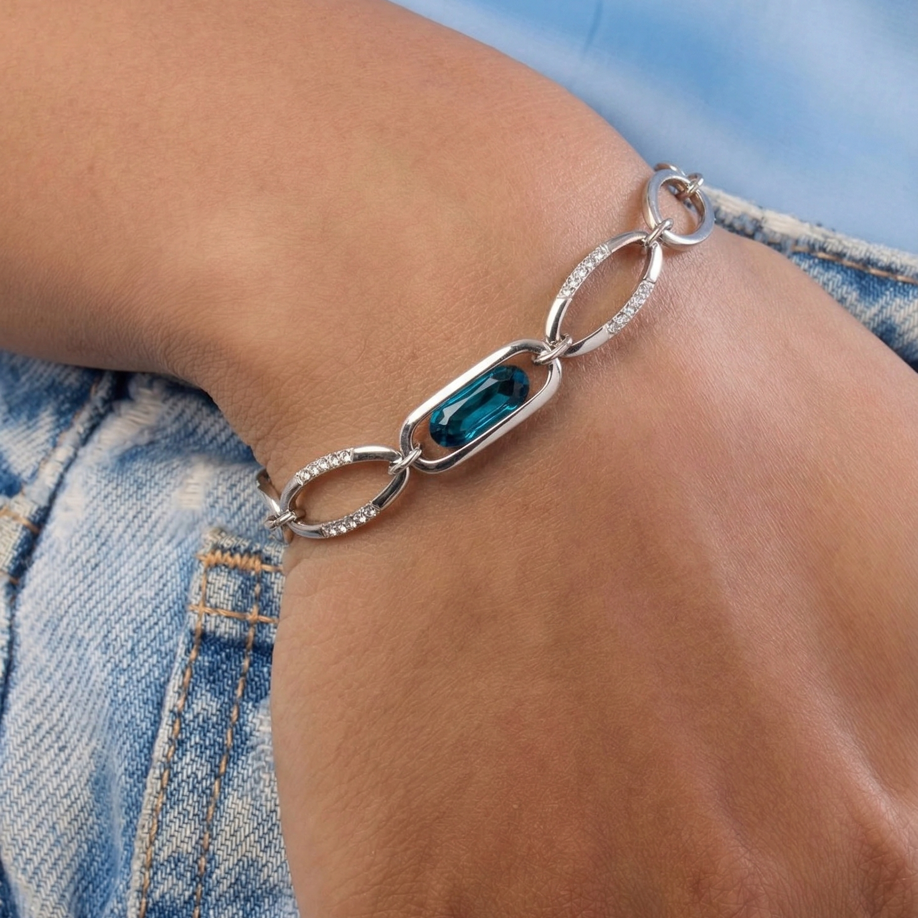 Silver bracelet with a blue gemstone on a wrist, wearing denim jeans.