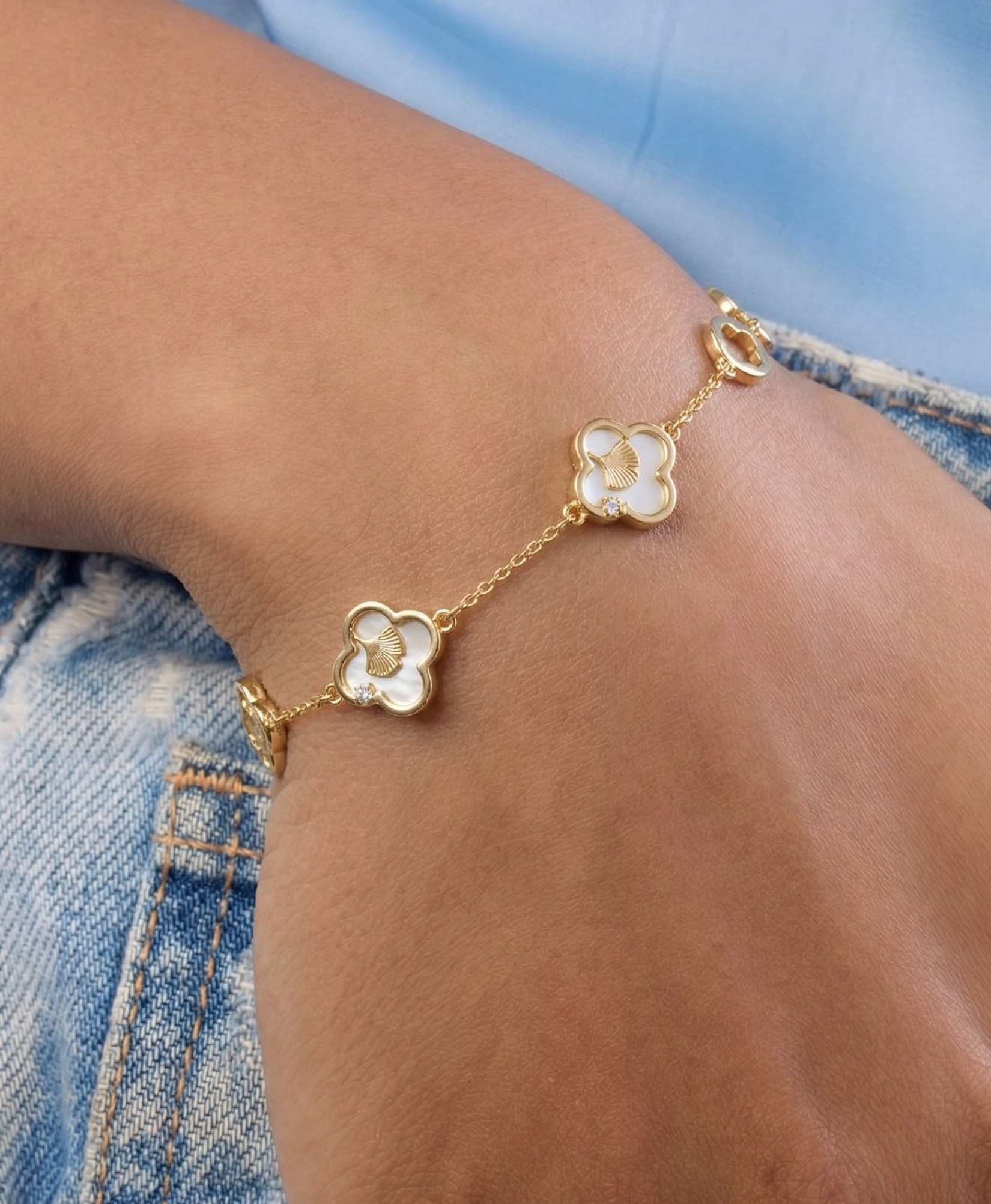 Gold bracelet with floral designs on a wrist against a denim background