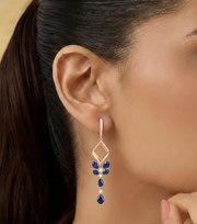Close-up of a woman wearing a diamond earring with blue gemstones.