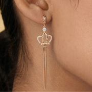 Rose gold crown-shaped earring worn by a person with dark hair.