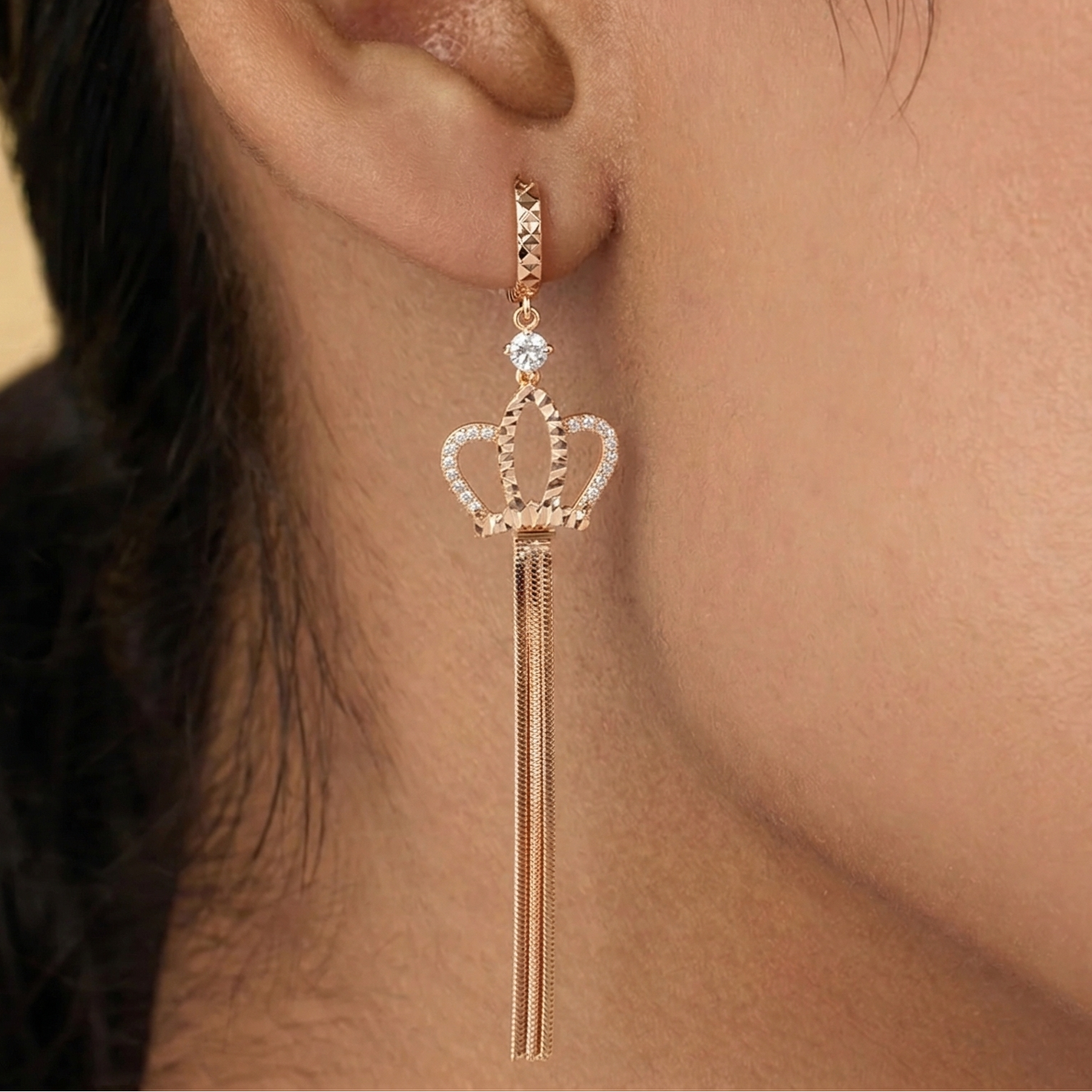 Rose gold crown-shaped earring worn by a person with dark hair.