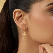 Close-up of a woman wearing a gold cross earring.