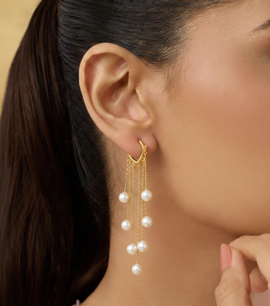 Close-up of a woman wearing gold earrings with pearl drops against a neutral background