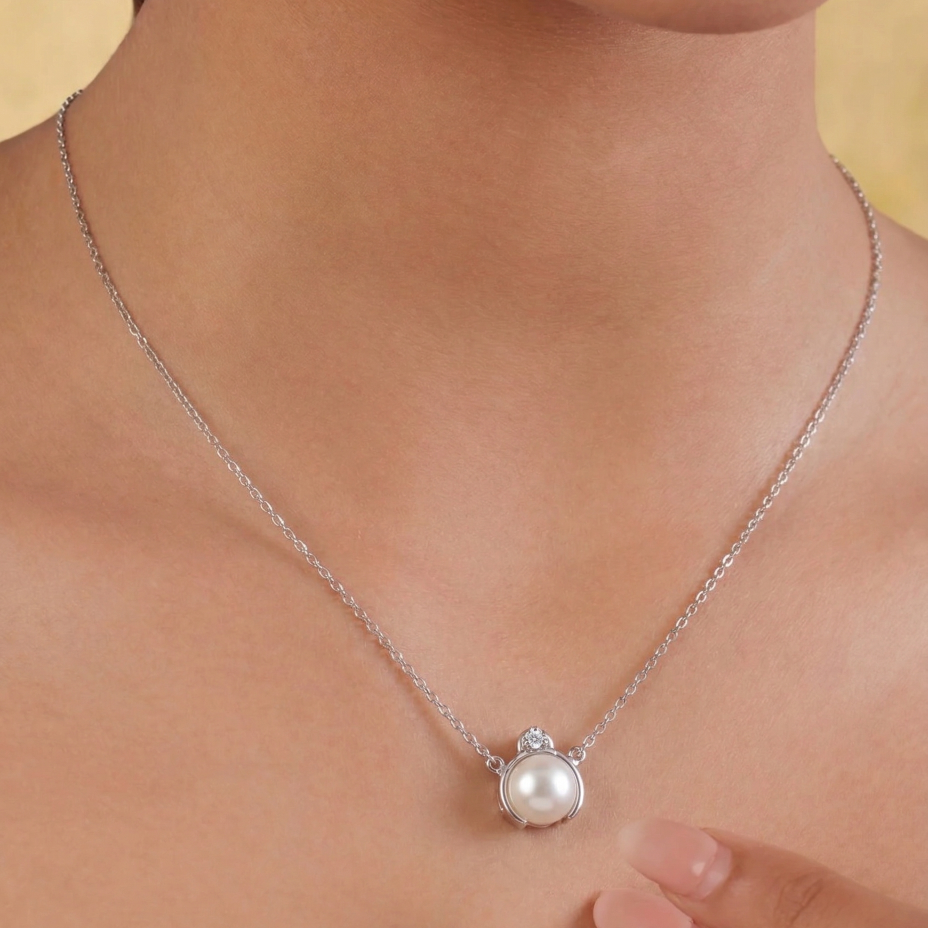 Pearl necklace with silver chain on a person's neck against a neutral background