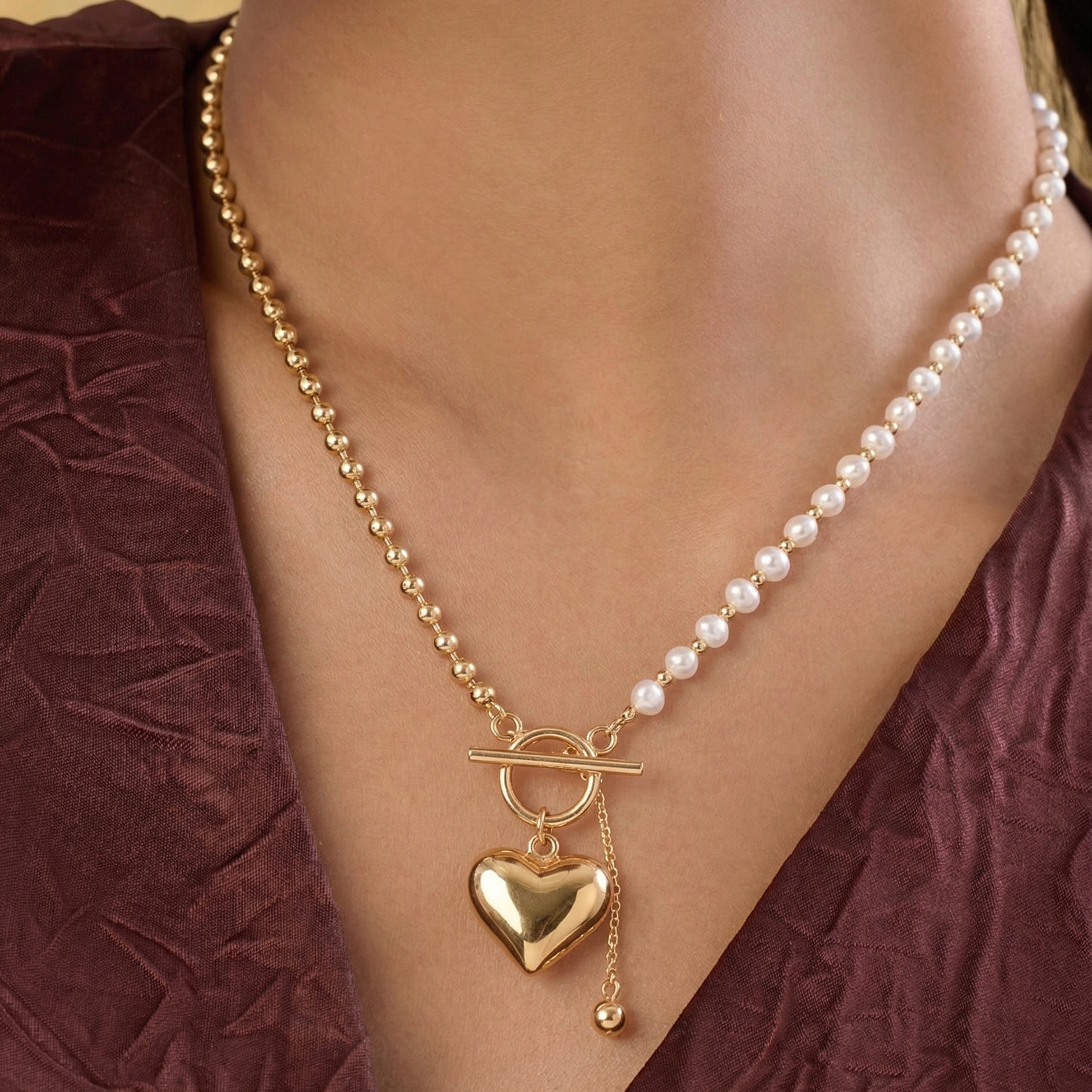 Necklace with a heart pendant on a person wearing a burgundy top.