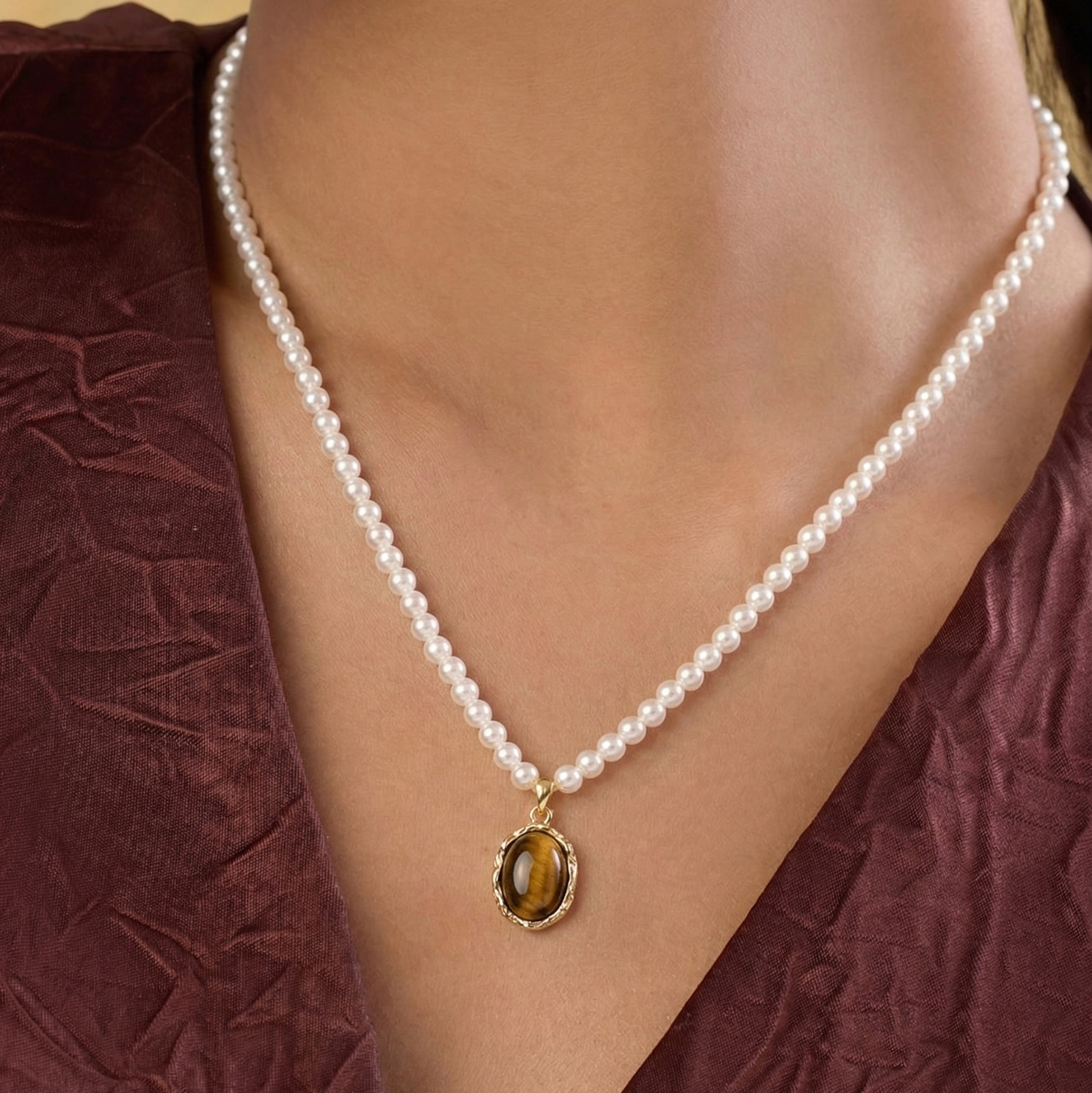 Pearl necklace with a gold pendant on a person wearing a maroon top.
