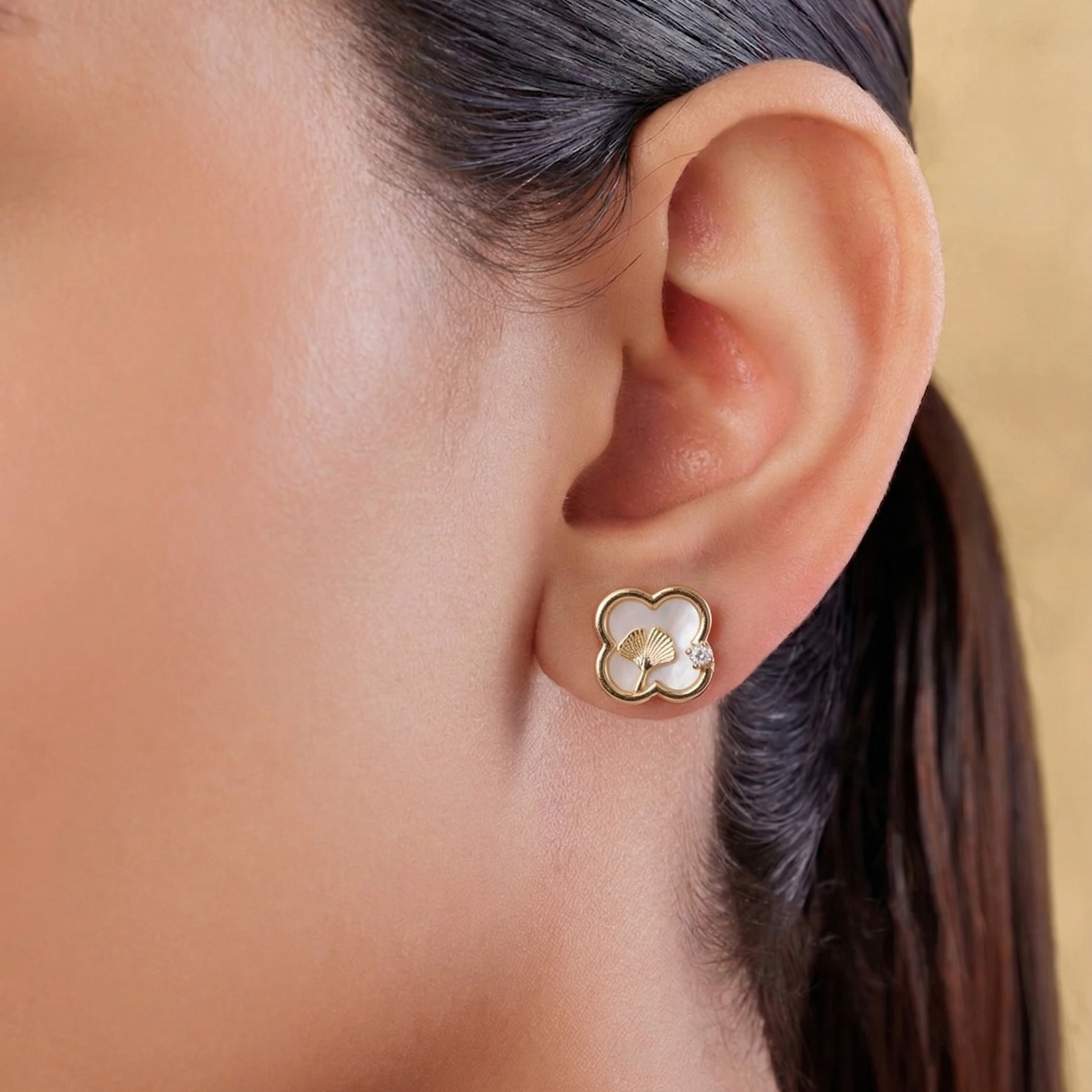 Close-up of an ear wearing a gold and pearl earring with a neutral background