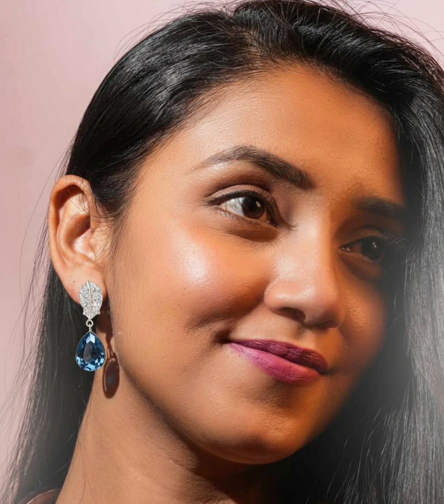 Close-up of a woman wearing a blue teardrop earring against a pink background