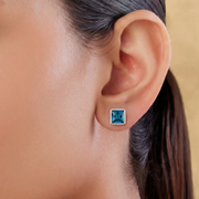 Close-up of an ear wearing a blue square stud earring with a neutral background
