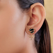 Close-up of an ear wearing a black heart-shaped earring with gold bow detail.