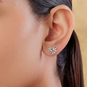 Close-up of an ear wearing a sun-shaped earring with a green gemstone.