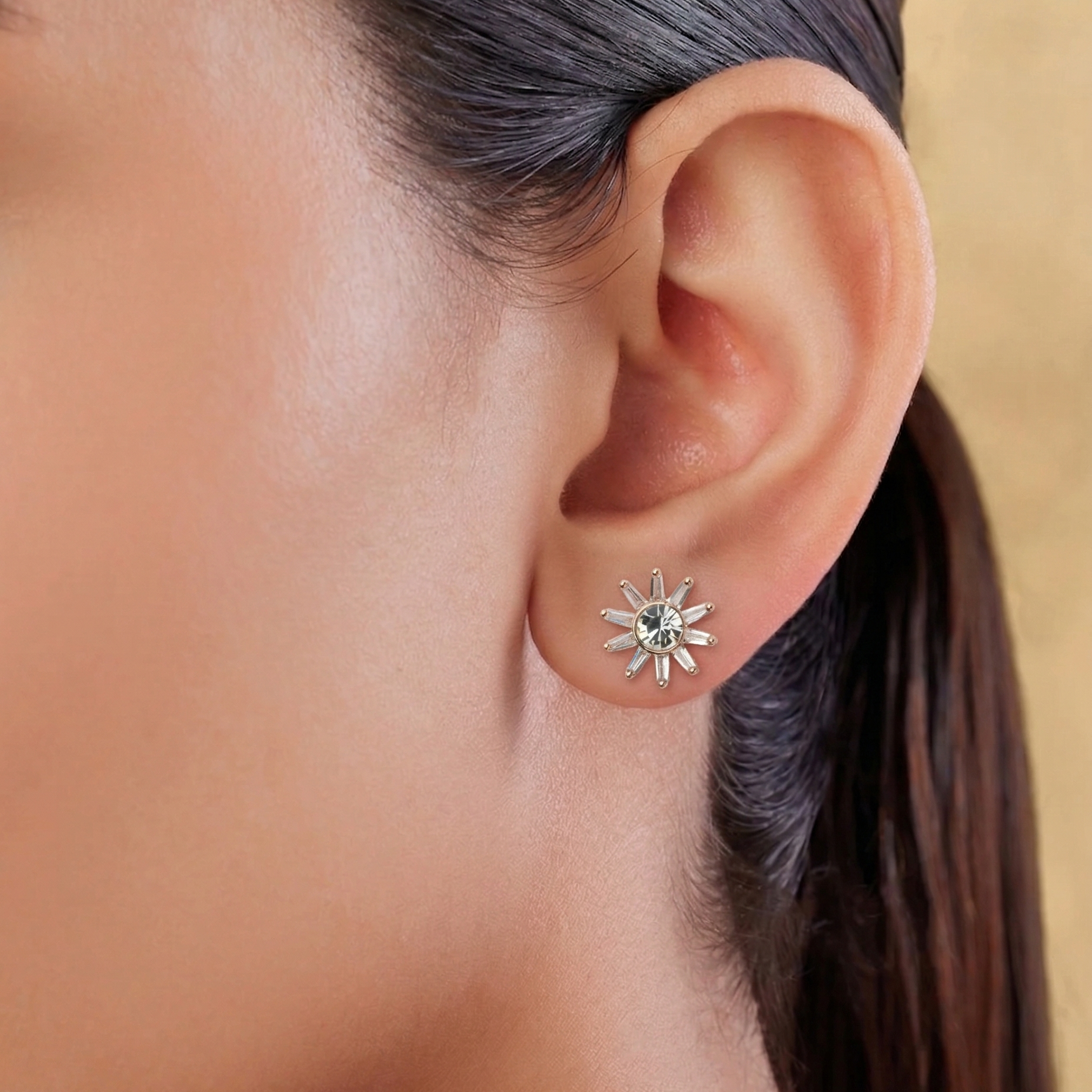 Close-up of an ear wearing a sun-shaped earring with a green gemstone.