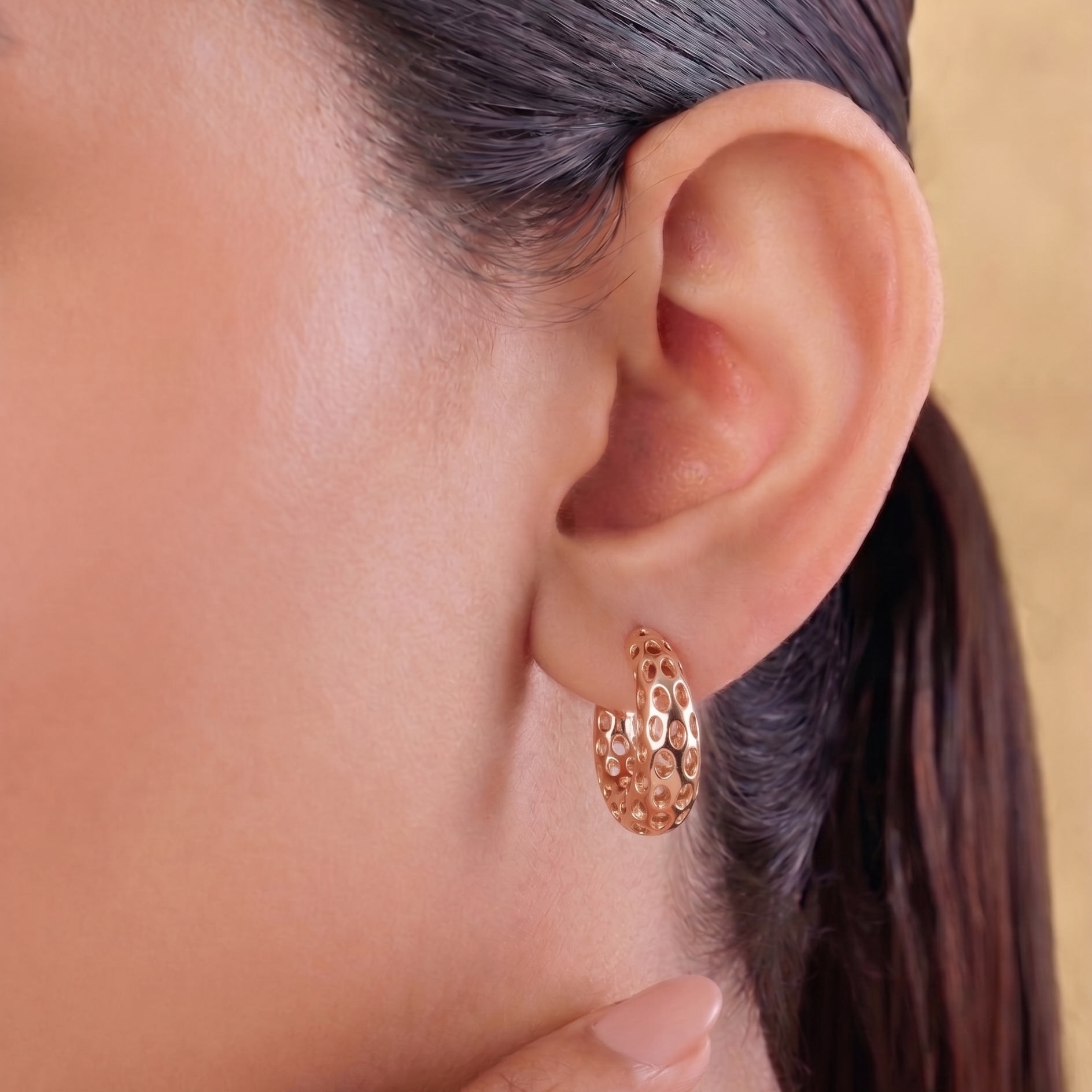 Close-up of an ear wearing a gold earring with a blurred background