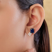 Close-up of an ear wearing a blue gemstone earring with a matching flower-shaped earring.