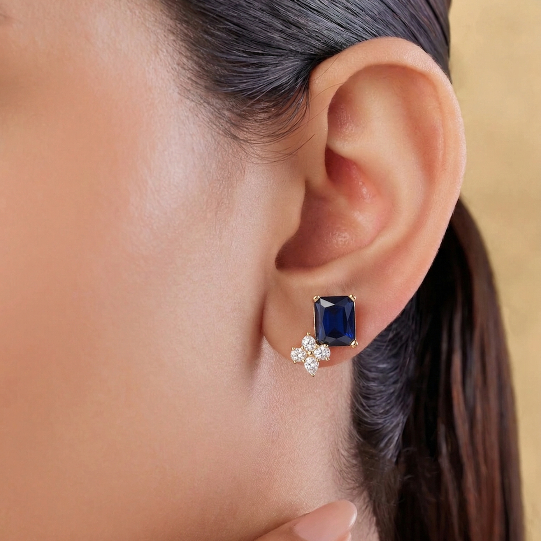 Close-up of an ear wearing a blue gemstone earring with a matching flower-shaped earring.