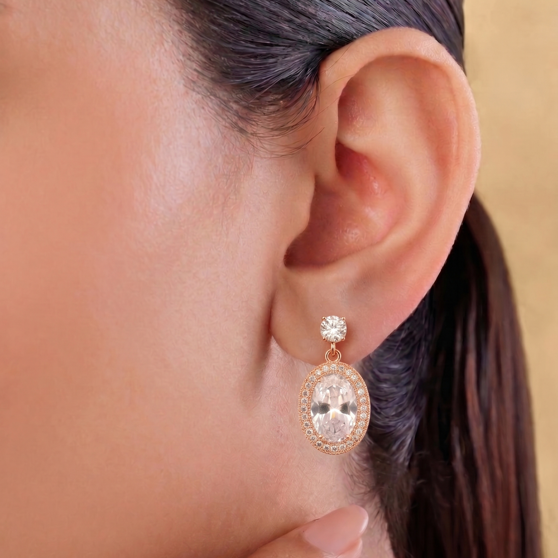 Close-up of an ear wearing a rose gold earring with a clear gemstone.