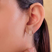 Close-up of an ear wearing a gold hoop earring with a neutral background