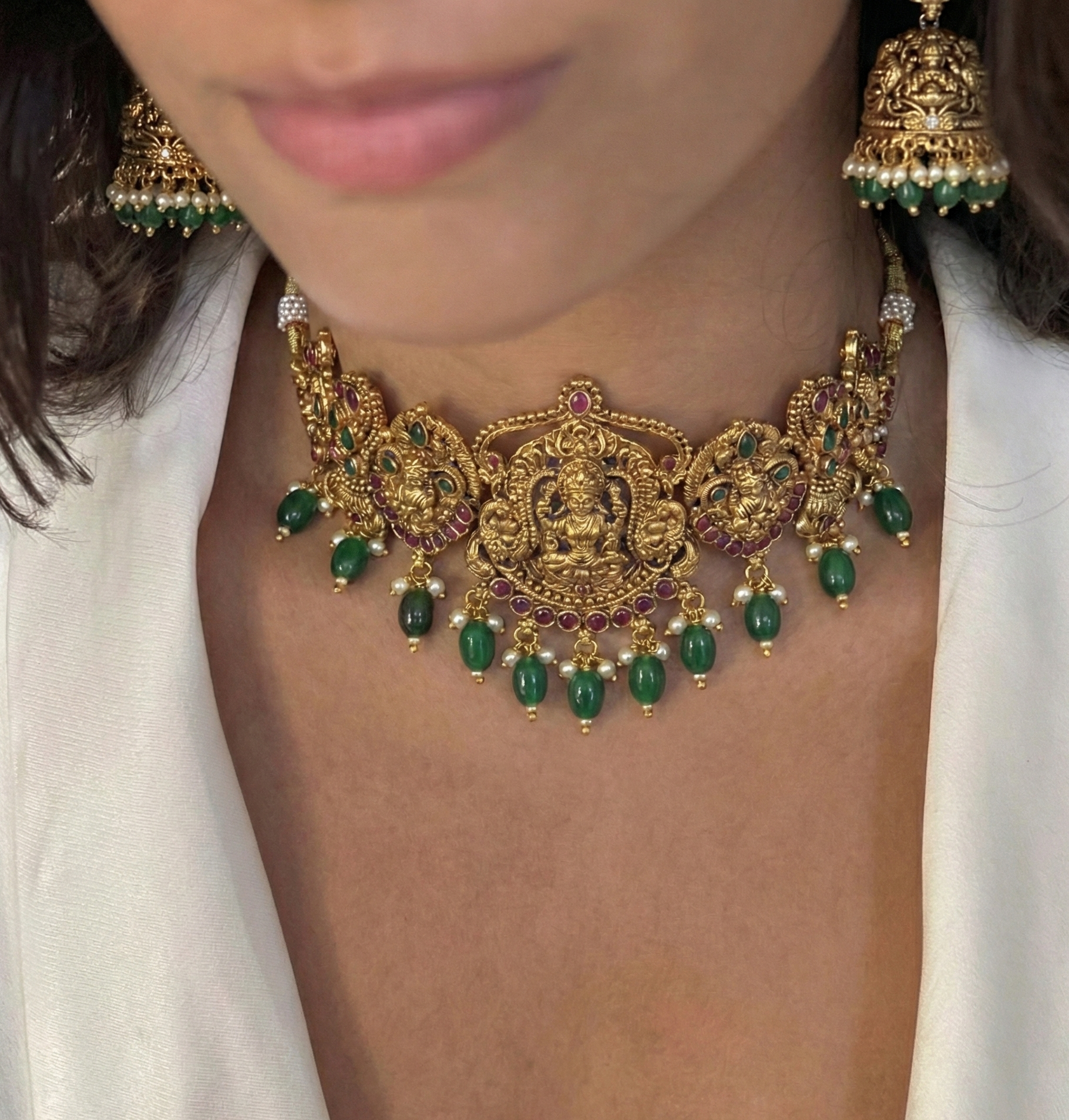 Close-up of a person wearing an ornate gold necklace with green gemstones and matching earrings.