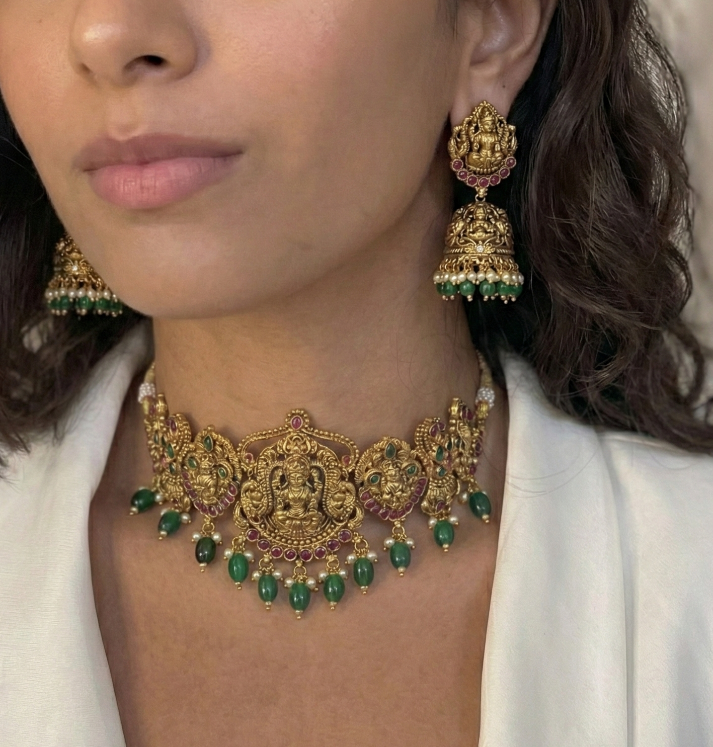 Woman wearing gold and green jewelry set with a white blazer