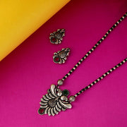 A set of oxidized silver jewelry including a mangalsutra necklace with a unique statement pendant adorned with magenta and green stones, and matching earrings, with a traditional black-beaded chain.