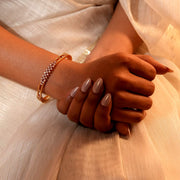 A  woman wearing single gold bangle bracelet with intricate diamond-like detailing.