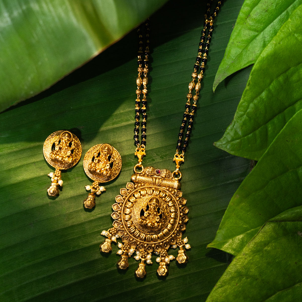 Gold necklace and earrings on green leaves