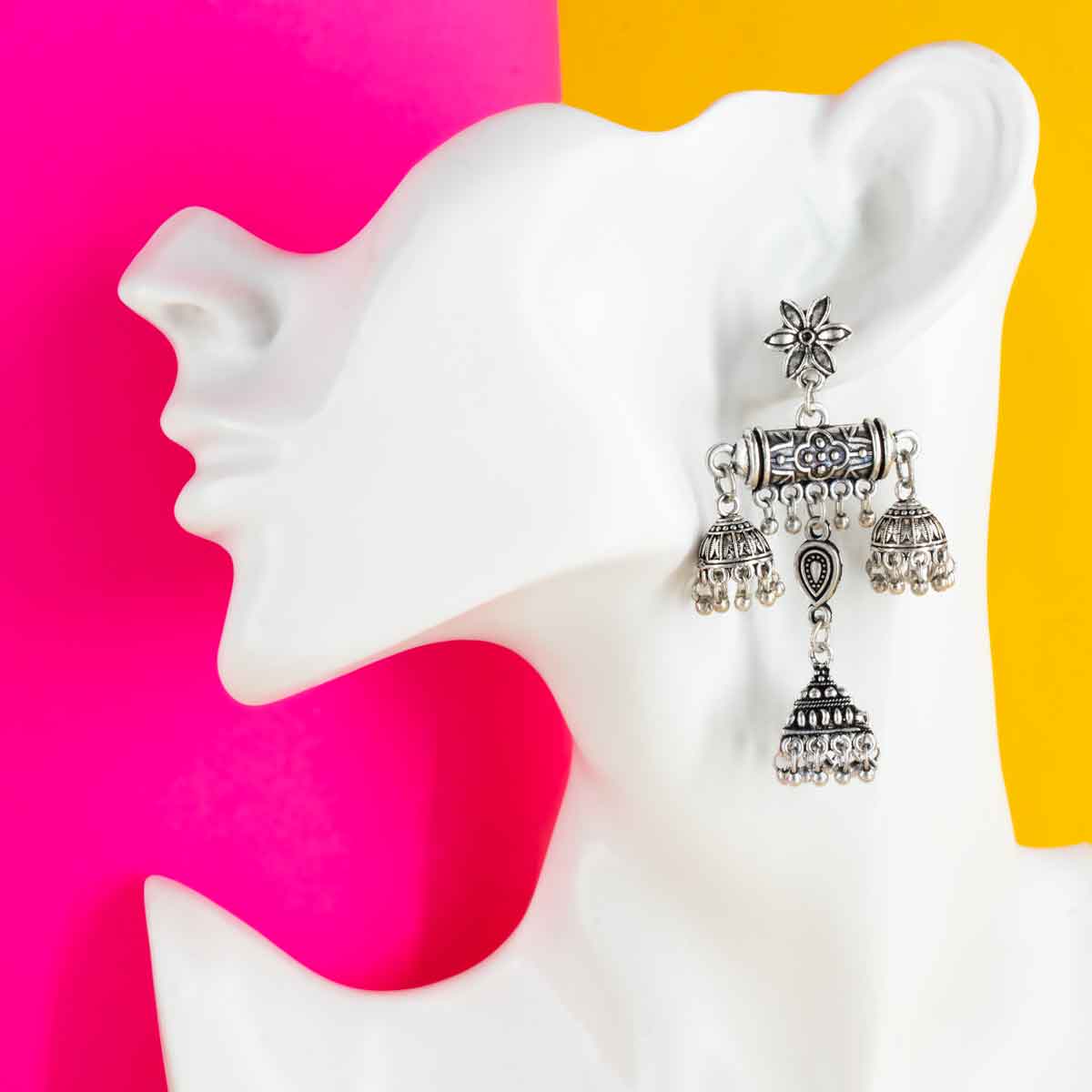 A pair of oxidised silver jhumka earrings with intricate design and multiple dangling elements on yellow and pink background. 